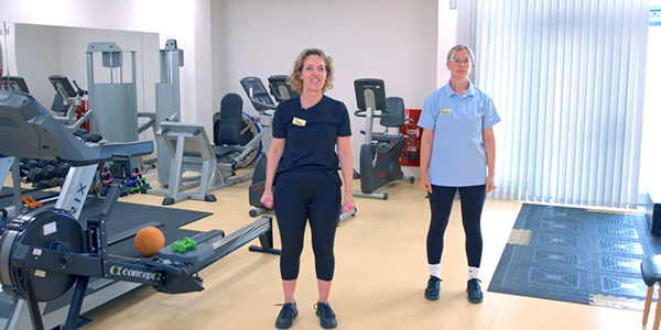 Screenshot of one of the videos showing two physiotherapists in a gym with one of them talking to camera. Click on this image to open the video playlist