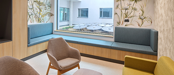 A consultation room with comfortable furniture, floral murals on the wall and a courtyard in the background with an art installation