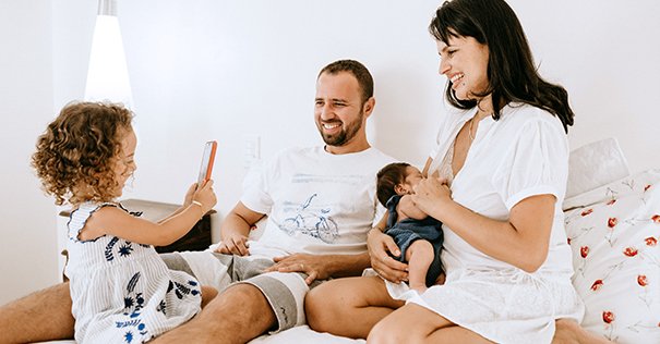 Family together on a bed with baby and todler using a mobile phone