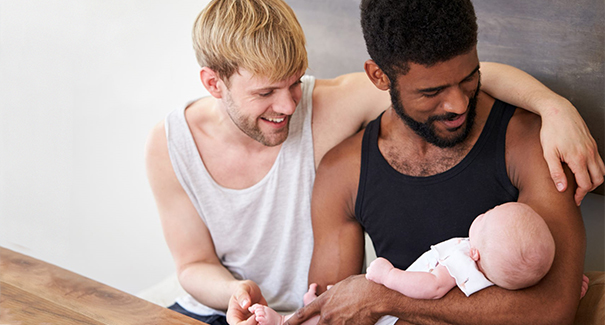 Two smiling men holding their baby