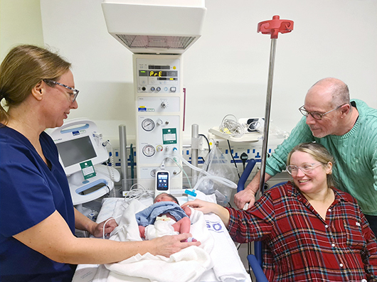 Baby George having the screening test with his parents by his side and a clinician administering the test