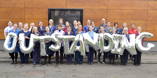 A picture of the Maternity team standing outside the Neonatal Intensive Care building holding up balloons that spell out the word Outstanding